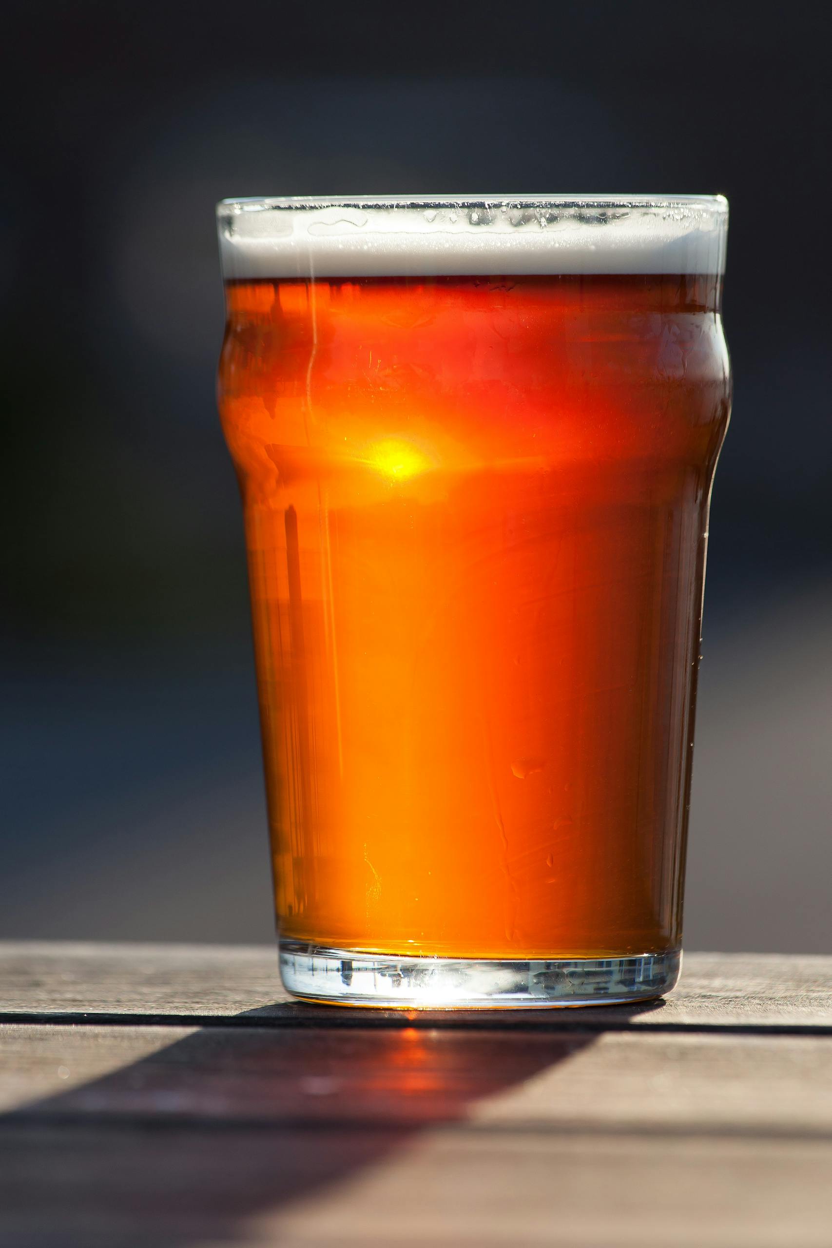 A refreshing pint of amber ale in sunlight on an outdoor table.